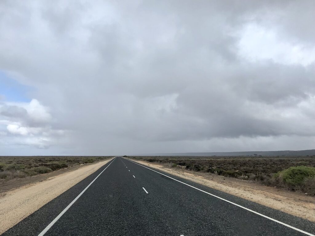 A long straight on the Eyre Highway, west of Eucla near Mundrabilla. A Rain shower in the distance.