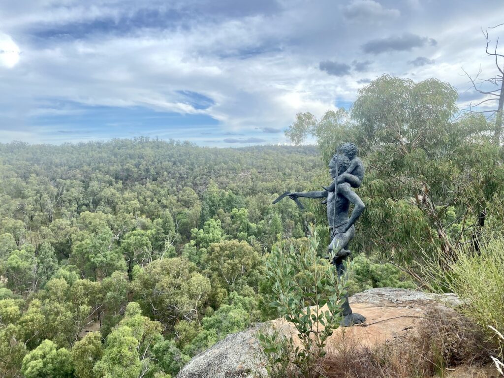 Dhayaanduul Waanda (First Lesson). Man with young boy in shoulders pointing down into Dandry Gorge. Sculptures In The Scrub, Pilliga Forest NSW.