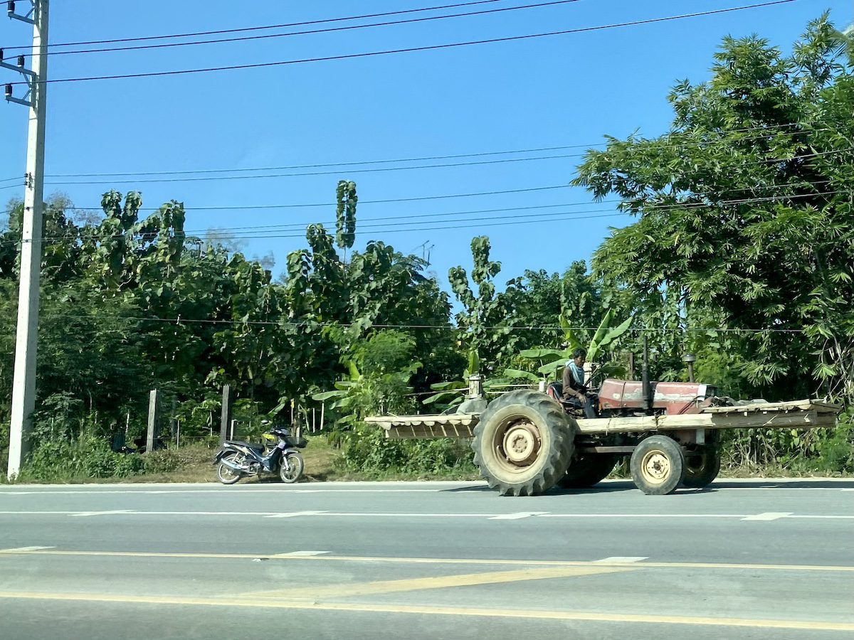 Driving in Thailand. Tractor driving along the side of a dual lane freeway.